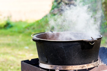 Steam over iron cauldron, meal is preparing in an iron pot outdoors. Camping in the nature and...