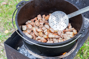 Meat is cooking in the pot on the fire for rice pilau outdoors. Camping in the nature and preparing food concept