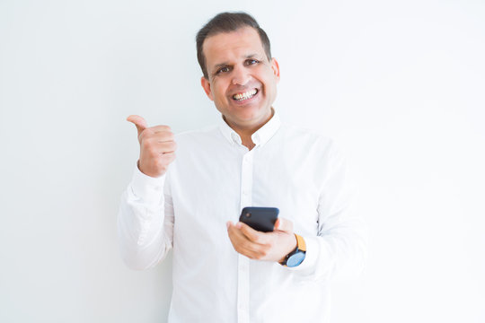 Middle age man using smartphone over white wall pointing and showing with thumb up to the side with happy face smiling