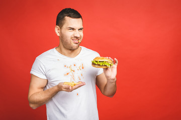 Funny hungry bearded man eating junk food. Excited young man greedily eating hamburgers isolated on...