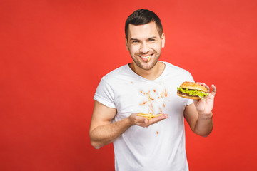 Funny hungry bearded man eating junk food. Excited young man greedily eating hamburgers isolated on red background.