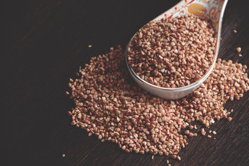 Part of buckwheat in a spoon and part scattered on a dark wooden table.