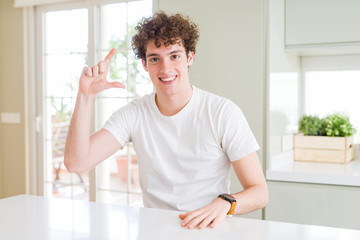 Young handsome man wearing white t-shirt at home smiling and confident gesturing with hand doing size sign with fingers while looking and the camera. Measure concept.