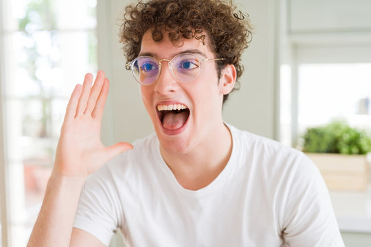 Young handsome man wearing glasses shouting and screaming loud to side with hand on mouth. Communication concept.