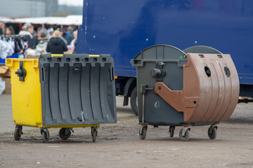two large bins at market with people and and blue van in the backround