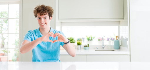 Wide shot of young handsome man at home smiling in love showing heart symbol and shape with hands. Romantic concept.
