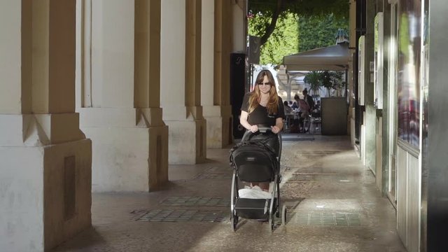 A girl in a black T-shirt walks with a black stroller through the old town Valetta in a hot day in slow motion