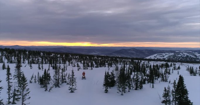 a guy on a mountain snowmobile rides on the background of a beautiful sunrise in a forest mountain valley with fields of snow. snowmobile traffic in the mountains. stock video footage. Aerial shot