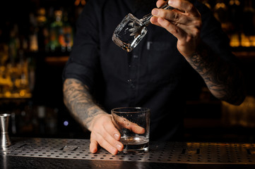 Bartender adding to an alcoholic drink in the glass a big ice cube