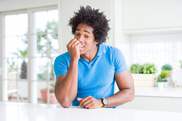 African American man at home looking stressed and nervous with hands on mouth biting nails. Anxiety problem.