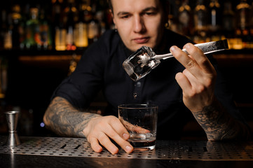 Attractive bartender adding to an alcoholic drink in the glass a big ice cube