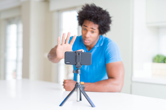 African American man doing online call with webcam using smartphone with open hand doing stop sign with serious and confident expression, defense gesture