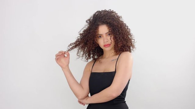 mixed race black woman with freckles and curly hair watching to the camera and curl her hair on finger. model touches her afro curly hair