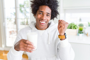 African American man holding and drinking glass of milk screaming proud and celebrating victory and...