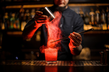 Professional bartender adding to an alcoholic drink a dried orange and powder