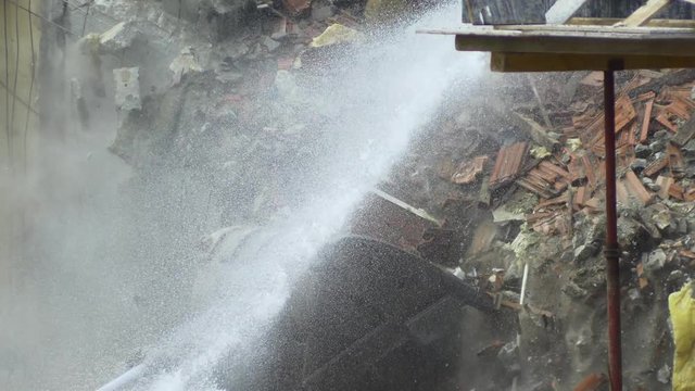 4K Building deconstruction with the heavy machinery. Tearing down old building on a construction site. Bulldozers turn old homes into rubble and dust fills the air. Digger using its bucket to demolish