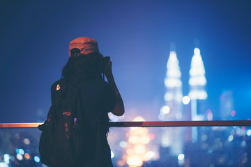 Travel and technology. Young woman taking photo with her smartphone of Petronas Twins Towers in Kuala-Lumpur at evening