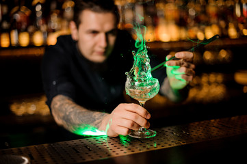 Man adding to a cocktail glass with dried orange a smoked cinnamon with tweezers