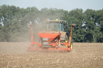Farmer with tractor with seeder, sowing (seeding) crops at agricultural field.