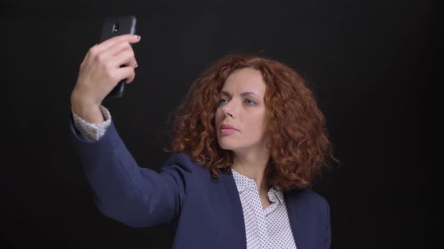 Closeup portrait of adult caucasian beautiful woman with red curly hair taking selfies on the phone in front of the camera