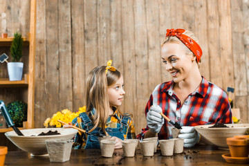 cheerful mother holding small shovel with ground and looking at cute daughter