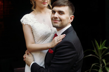 Beautiful romantic newlywed couple hugging near flower bouquets at luxury french restaurant outdoors, emotional blonde bride being embraced by handsome groom portrait