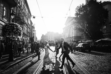 elegant happy wedding couple running and laughing in sunlight in city streets at evening in european town. luxury bride and groom having fun. romantic sensual moment. black white photo