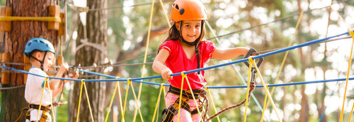 Little beautiful girl climbs on rope harness in summer city park.