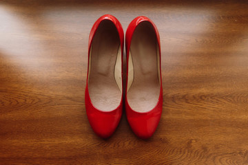 Stylish red women's shoes on wooden floor, elegant bride's shoes closeup on rustic background, morning wedding preparation