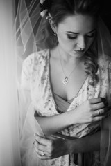 Beautiful bride looking out of window, morning wedding preparation, sensual blonde woman in sexy robe and veil portait in room, face closeup