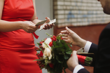 Handsome groom in elegant black suit and wedding bouquet paying for the bride to bridesmaid, slavic...