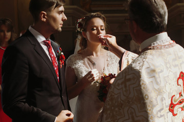 Beautiful bride and handsome groom kissing wedding rings, spiritual christian couple kissing gold rings during wedding ceremony in church, romantic moment