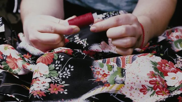 people and home concept - female hands, reeling the red thread on the spool