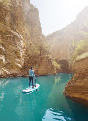 Man Paddling on SUP board into a canyon.