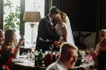 Newlywed couple kissing at wedding reception in restaurant, bride and groom first kiss in front of...
