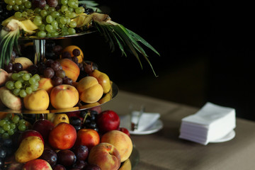 Delicious, healthy fruit tower at wedding reception dessert table close-up, brown tablecloth background, peaches, grapes, pineapple and pear meal at wedding catering