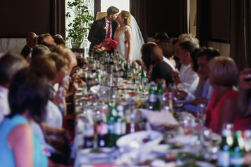Newlywed couple kissing at wedding reception in restaurant, bride and groom first kiss in front of friends and family, romantic moment, marriage concept