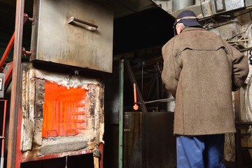 A man is a worker, pulls out the hot parts from an electric furnace for hardening metal. A man at dangerous work with high temperature in a heavy industry at the valve manufacturing plant