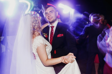Evening dance party - newlywed bride and groom dancing at wedding reception ballroom, surrounded by colorful neon lights