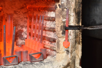 Worker pulls out the heated parts with tongs from an electric furnace for hardening metal. Dangerous work with high temperatures in heavy industry in a valve manufacturing plant