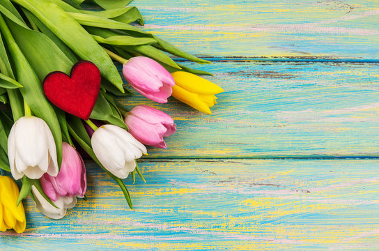 Bunch of fresh flowers with red wooden heart on the colorful background