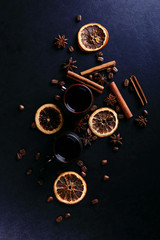 A cup of coffee, star anise, cinnamon, dried orange and coffee beans on a dark kitchen countertop. Fragrant spices for a drink, close-up, top view, flat ley.