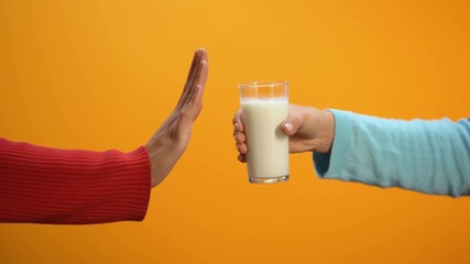 Female refusing to drink milk showing stop gesture on bright background, health