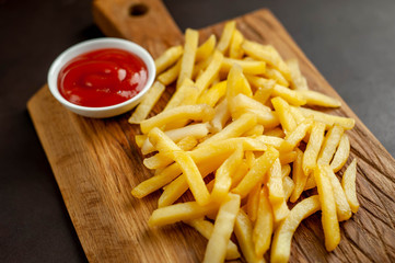 French fries with ketchup on a cutting board, background is concrete
