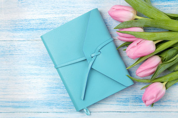 Beautiful bouquet of pink tulips flowers and a blue notebook on a blue wooden background. view from above. Spring. holidays.