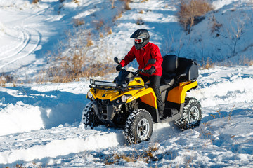 Attractive young man in red warm winter clothes and black helmet on the ATV 4wd quad bike stand in heavy snow with deep wheel track. Moto winter sports. © Screaghin