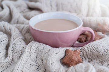 Cup of coffee with milk and star shaped ginger cookies on warm knitted beige blanket.