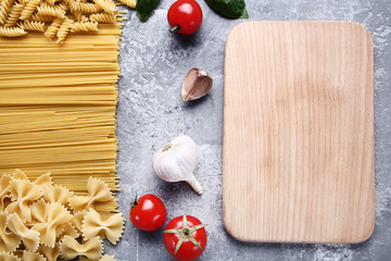 Dofferent pasta with tomatoes, garlic and cutting board on wooden table