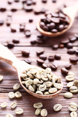 Green and brown coffee beans in spoons on wooden table