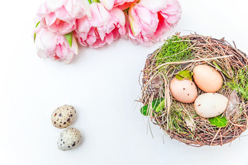 Spring greeting card. Easter eggs in nest and pink fresh tulip flowers bouquet on rustic white wooden background. Easter concept. Flat lay top view copy space. Spring flowers tulips